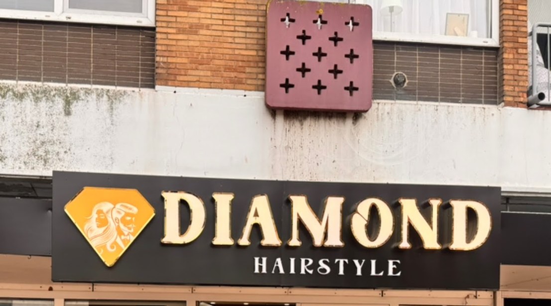 De gevel met het verlichte bord DIAMOND HAIRSTYLE en het wijnrode paneel met kruisjes erboven