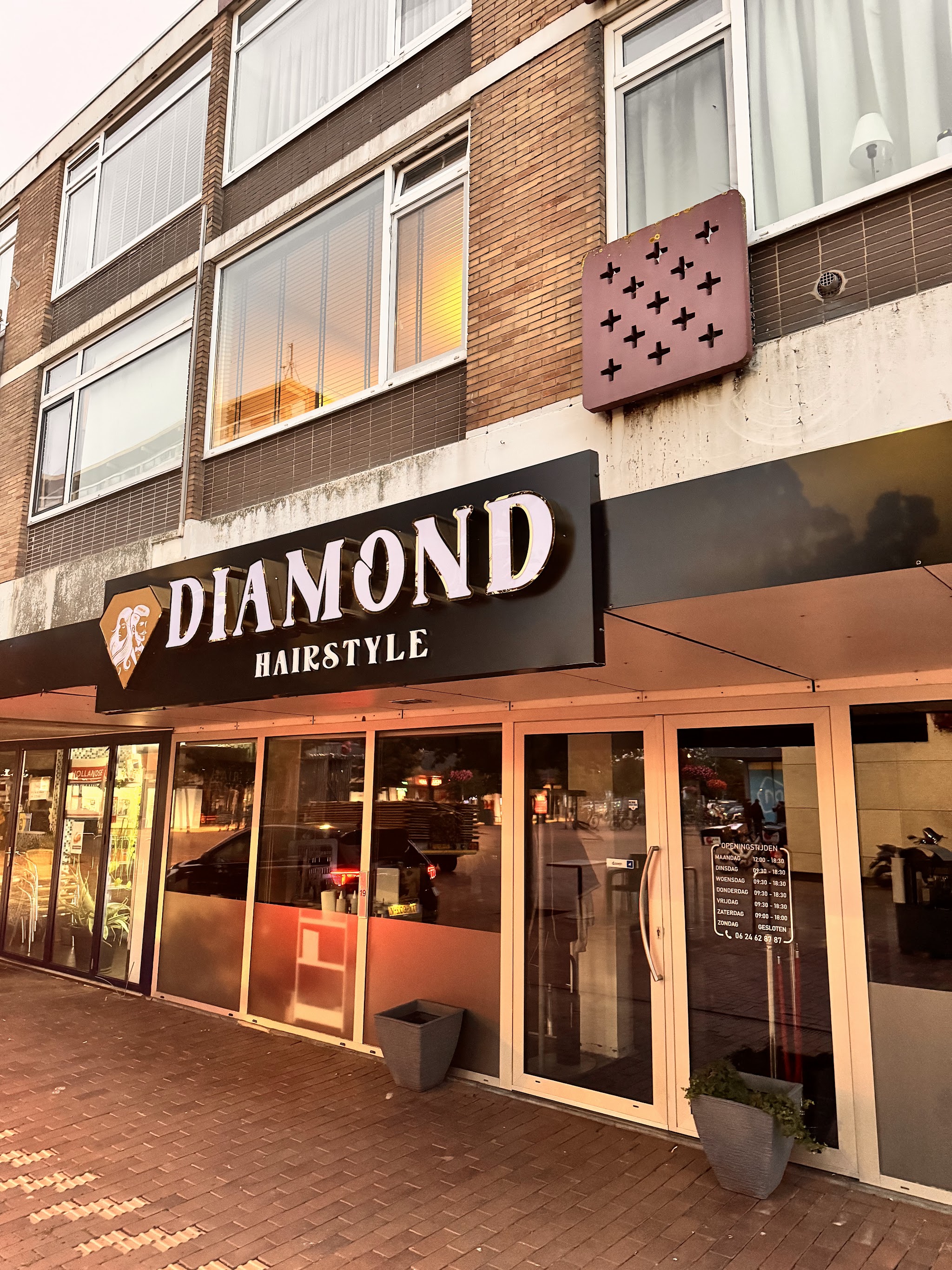De winkelpui van Diamond Hairstyle in de avond, met het verlichte bord boven de ramen